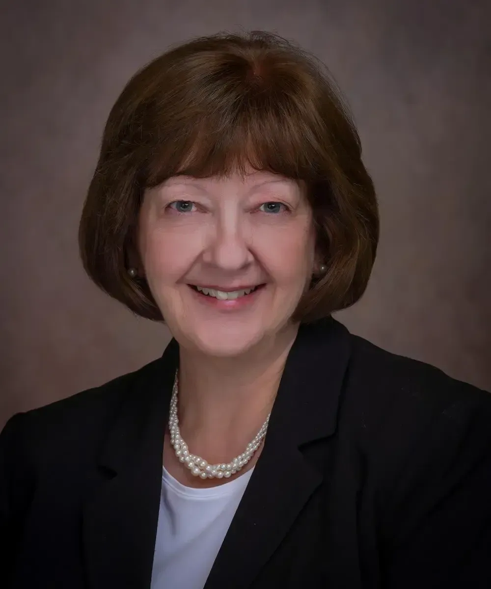 Julie Mitchell in a blue shirt and necklace is smiling in a circle.