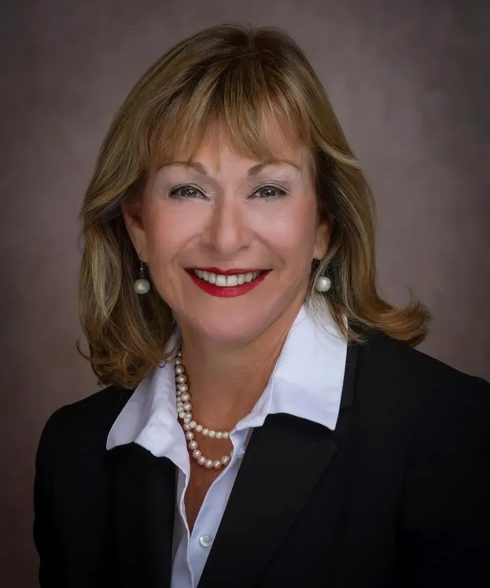 Julie Mitchell in a blue shirt and necklace is smiling in a circle.