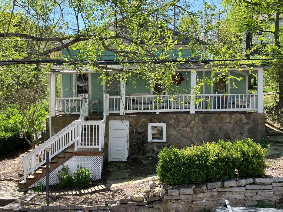 A house with a large porch and stairs is surrounded by trees.