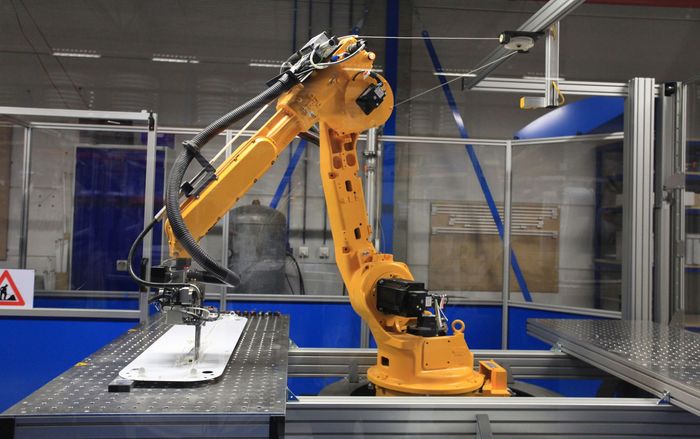 Braccio robotico giallo al lavoro in una fabbrica, mentre manipola un oggetto su un tavolo.