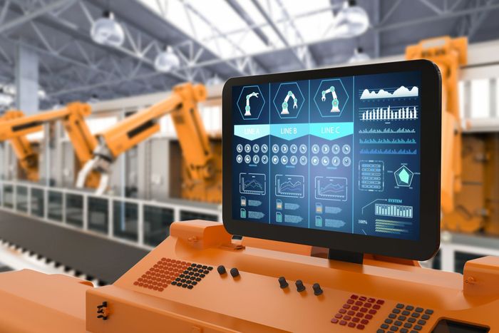 Pannello di controllo arancione con schermo che visualizza i dati, in una configurazione di fabbrica con bracci robotici.