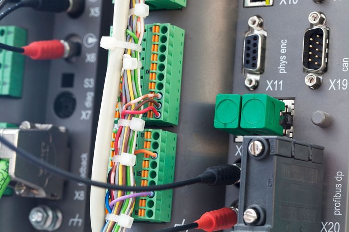 Primo piano del pannello di controllo industriale con morsettiere, fili e connettori verdi, che mettono in mostra i componenti elettronici.