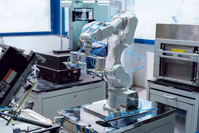 Braccio robotico in un laboratorio, mentre manipola oggetti, con vari macchinari e attrezzature sullo sfondo.