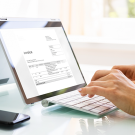 A person is typing on a laptop with an invoice on the screen.