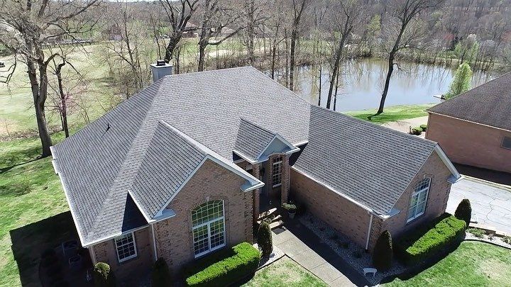 Aerial view of a brick house with gray roof near trees and a pond