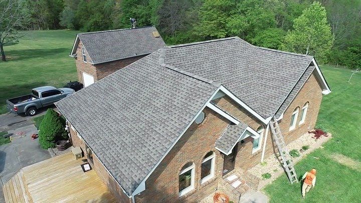 Aerial view of a brick house with a gray roof, ladder on the side, and a truck in the driveway.