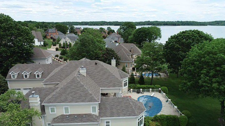 Aerial view of lakeside houses with gray roofs, trees, and a backyard pool near the water