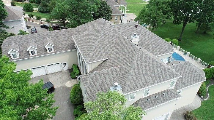 Aerial view of a large gray-roofed suburban house surrounded by trees and a lawn