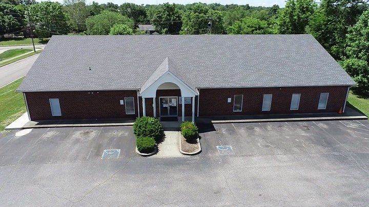 Brick building with gray roof and central entrance, viewed from above across an empty parking lot