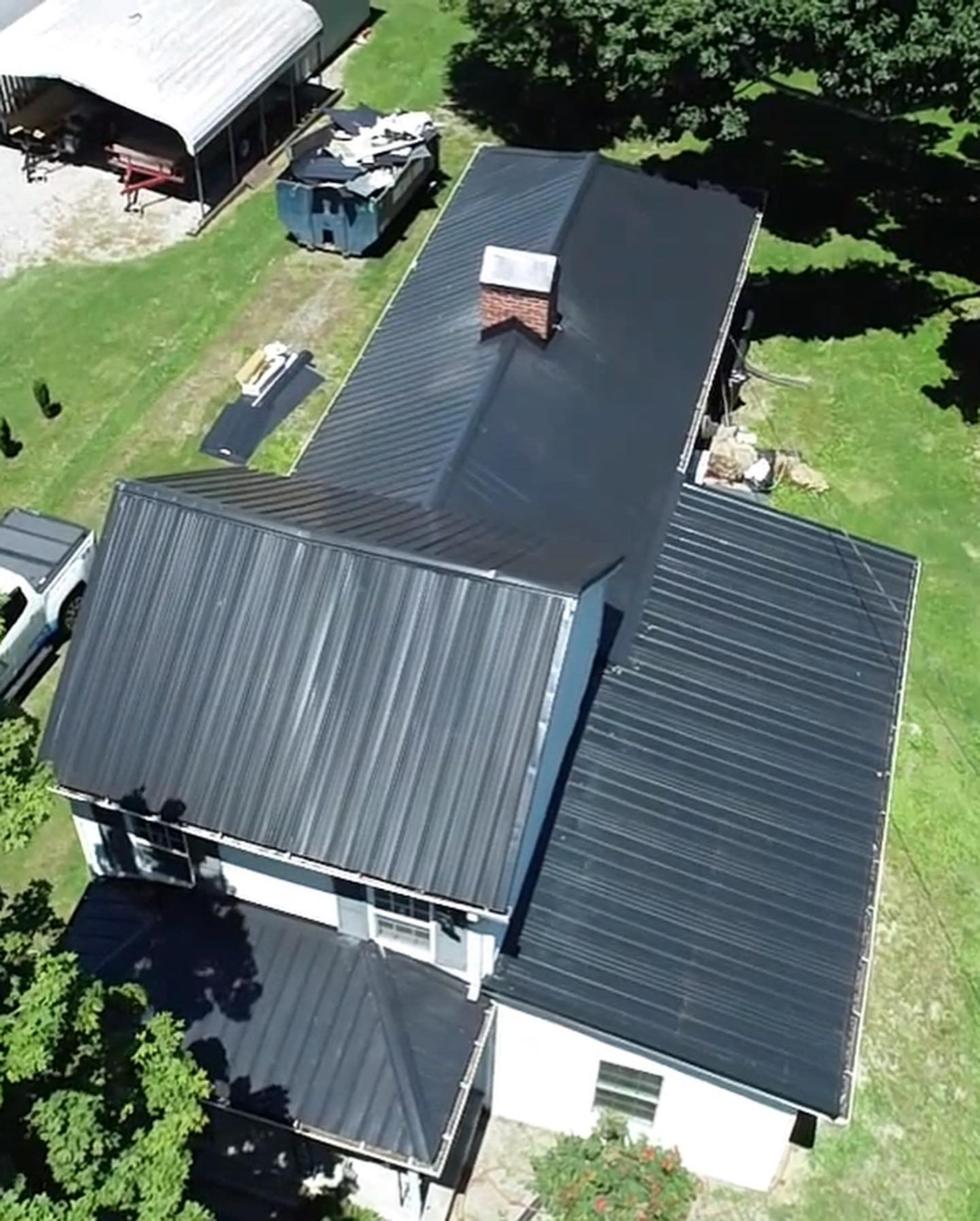 Aerial view of a house with a black metal roof surrounded by green lawn and trees.
