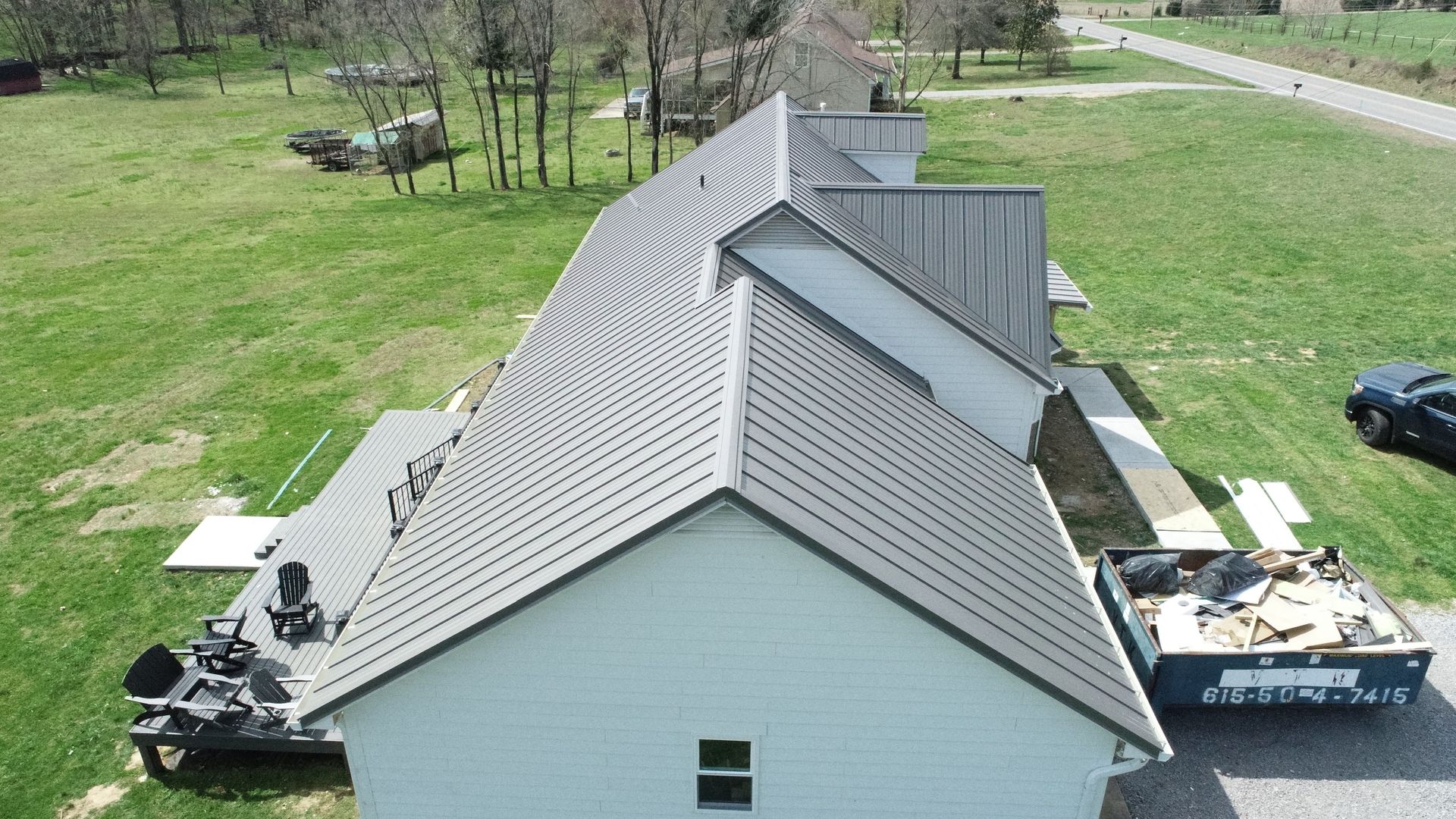 Aerial view of a house roof with dark gray shingles and white siding, surrounded by a grassy yard.
