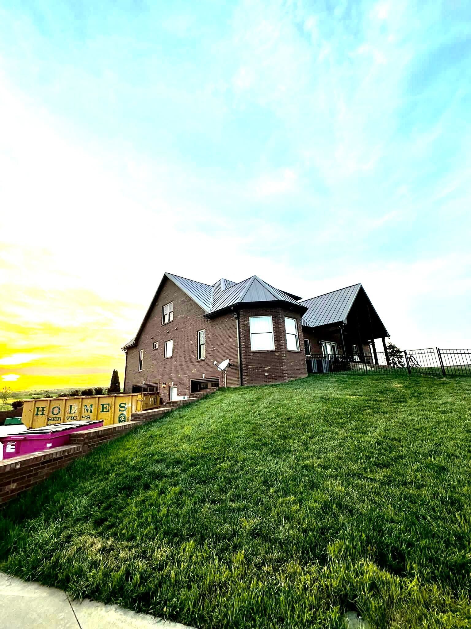 Brick house on a grassy hill at sunset, with a bright blue sky and yellow glow on the horizon