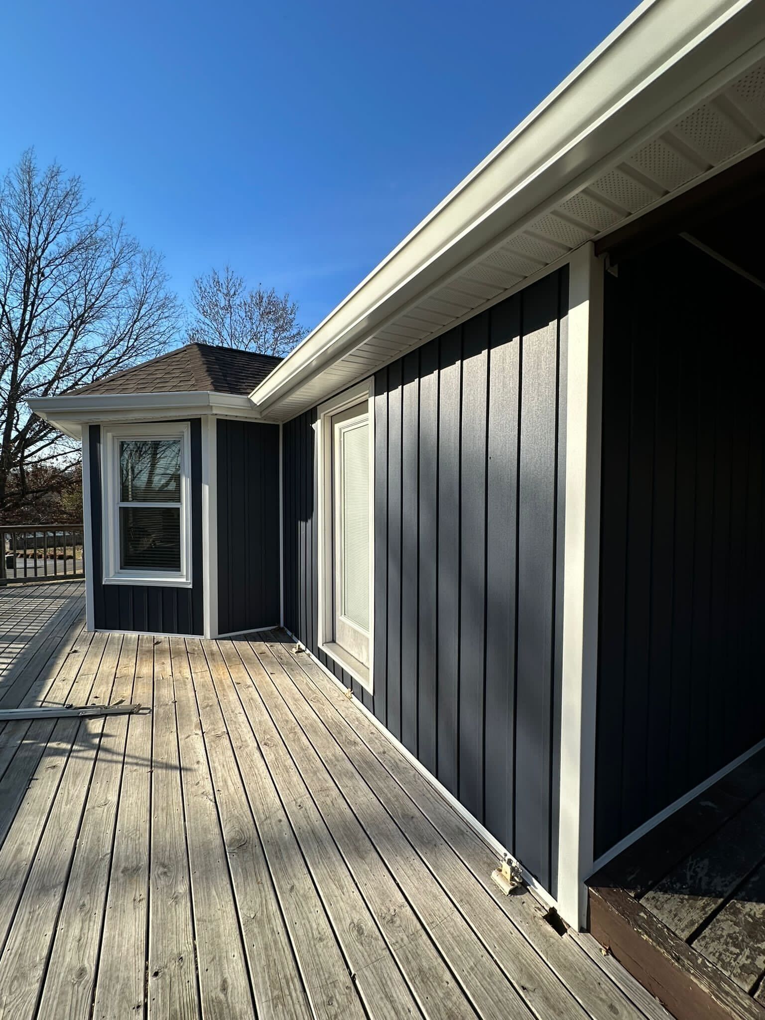 Covered wooden walkway beside a dark gray house under a clear blue sky
