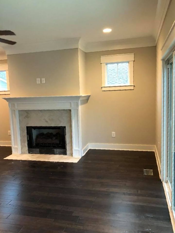 Empty living room with dark hardwood floors, beige walls, a white fireplace, and small windows.