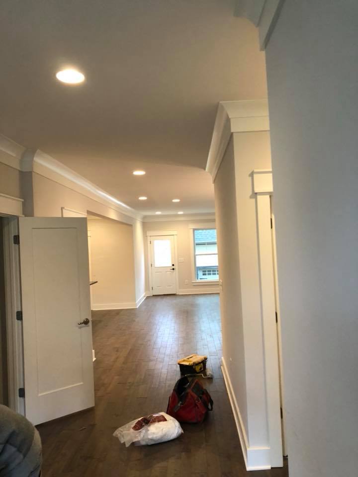 Empty hallway with white walls, recessed lights, wood floors, and bags on the floor near an open door.
