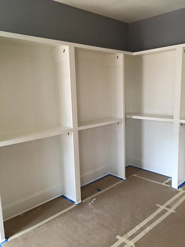 Built-in white closet shelves and hanging rods in an empty room with gray walls and carpet.