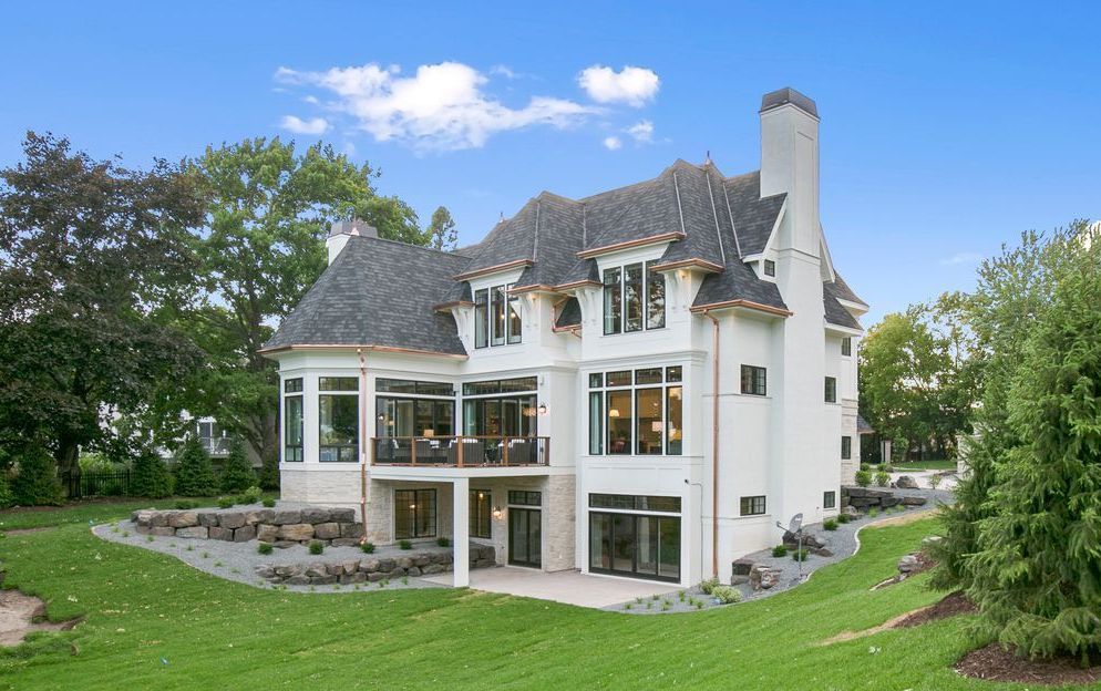 Large white two-story house with balconies and a steep gray roof, surrounded by a green lawn and trees