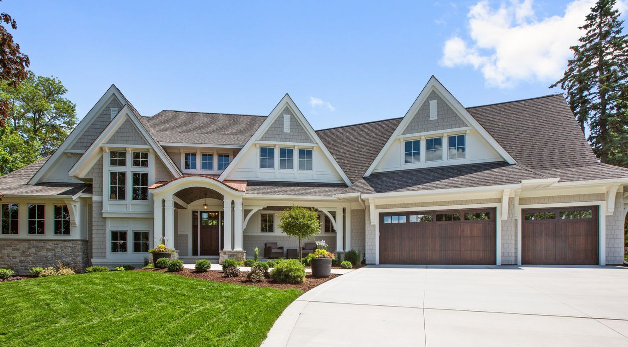 Large suburban house with gray roof, white trim, and a wide driveway under a blue sky