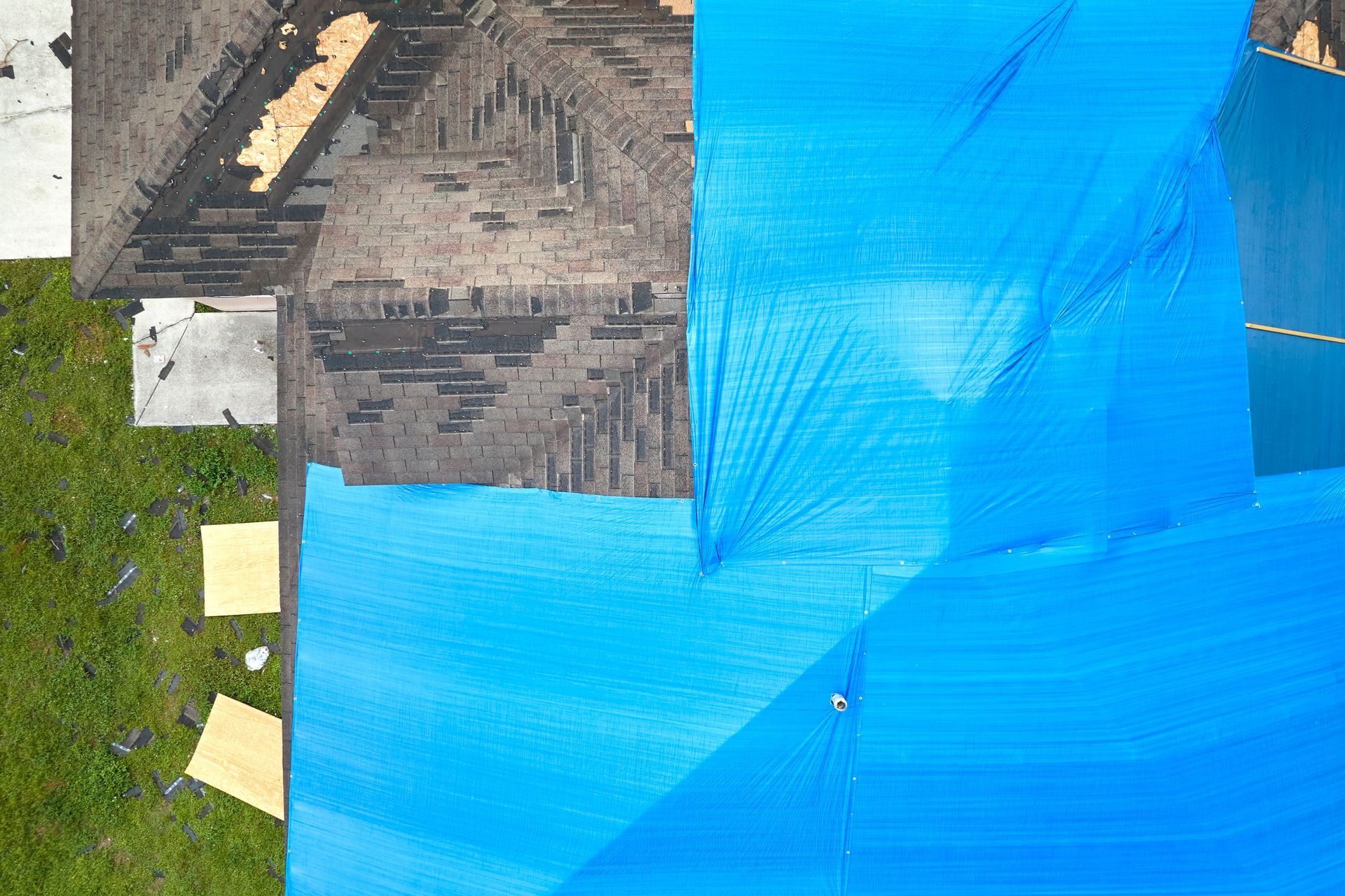 Aerial view of blue tarps covering a yard beside a rooftop and patches of grass.