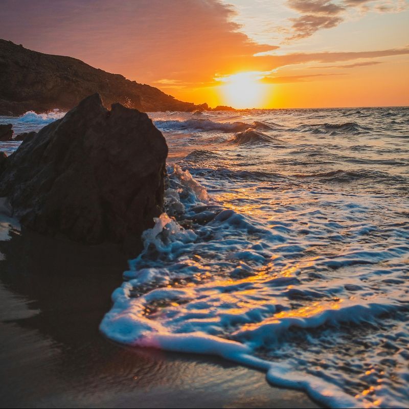 A sunset over the ocean with waves crashing on the shore