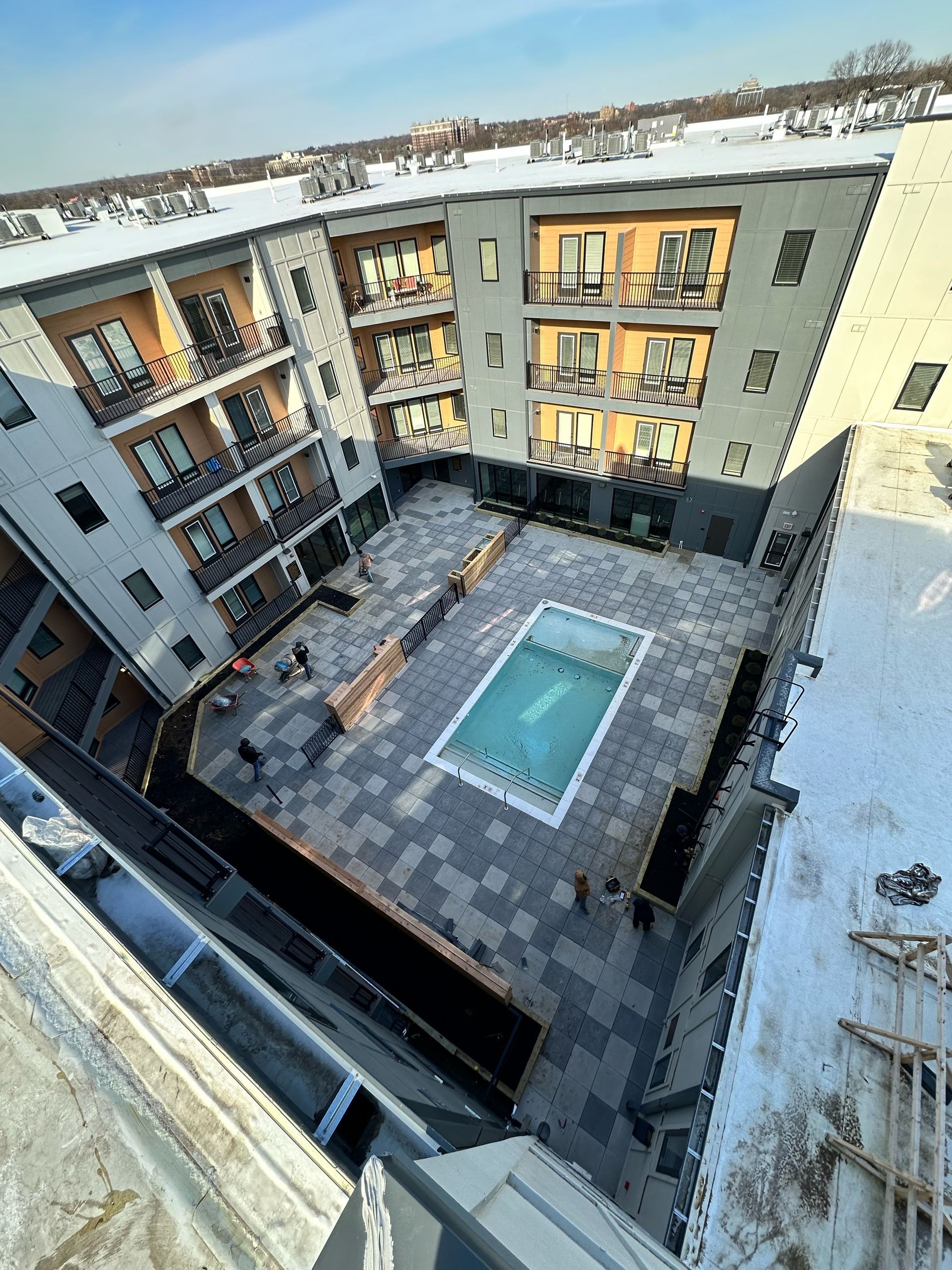 An elevated view of a multi-story apartment building courtyard featuring a central swimming pool surrounded by snowy patios.