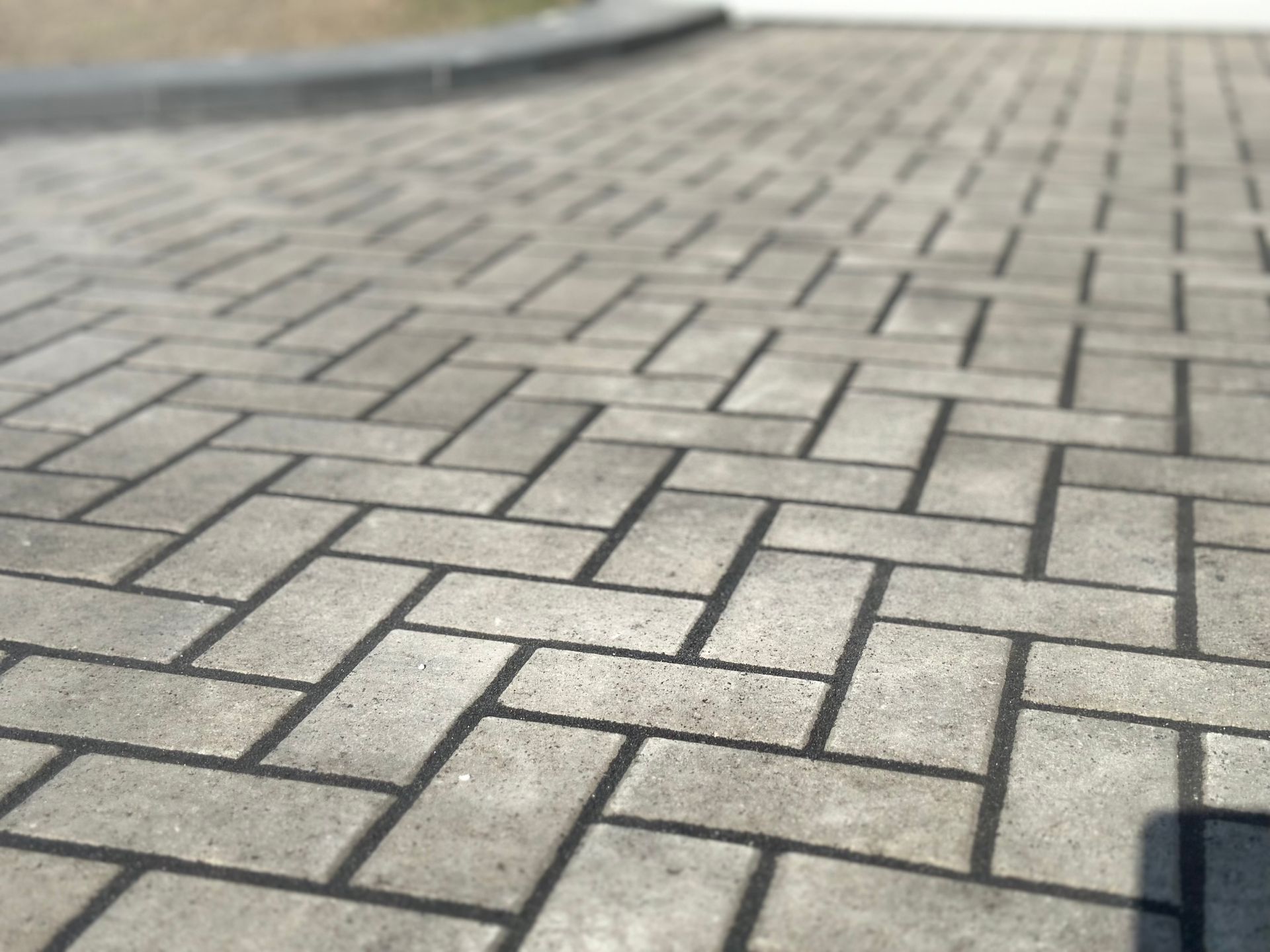 A close-up, angled view of a light gray concrete paver driveway arranged in a herringbone pattern.