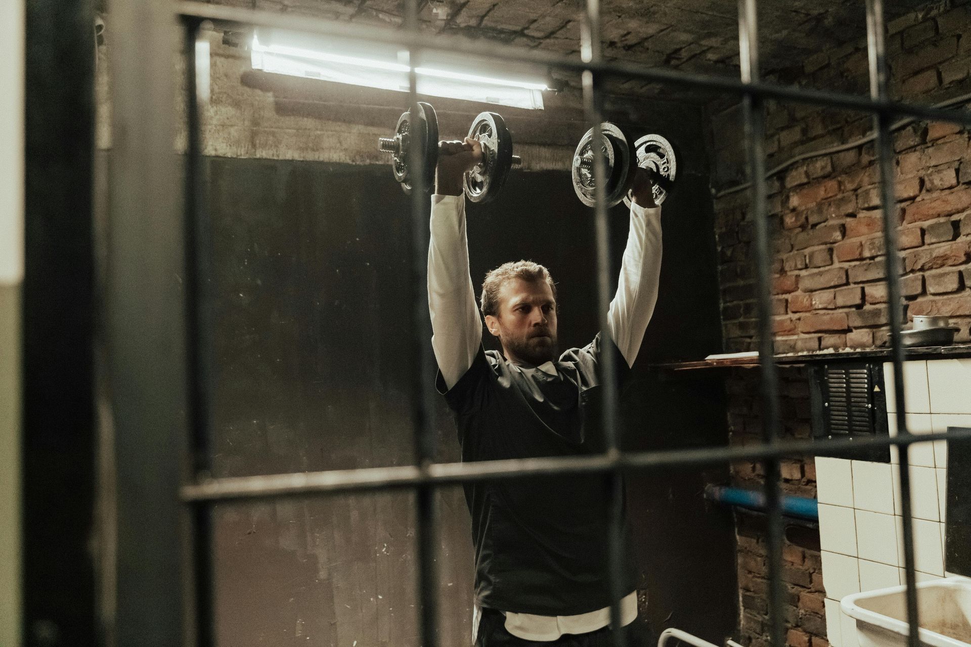 Een persoon zit in een sportschool en gebruikt een overhead press-machine, met de armen omhoog gestrekt.