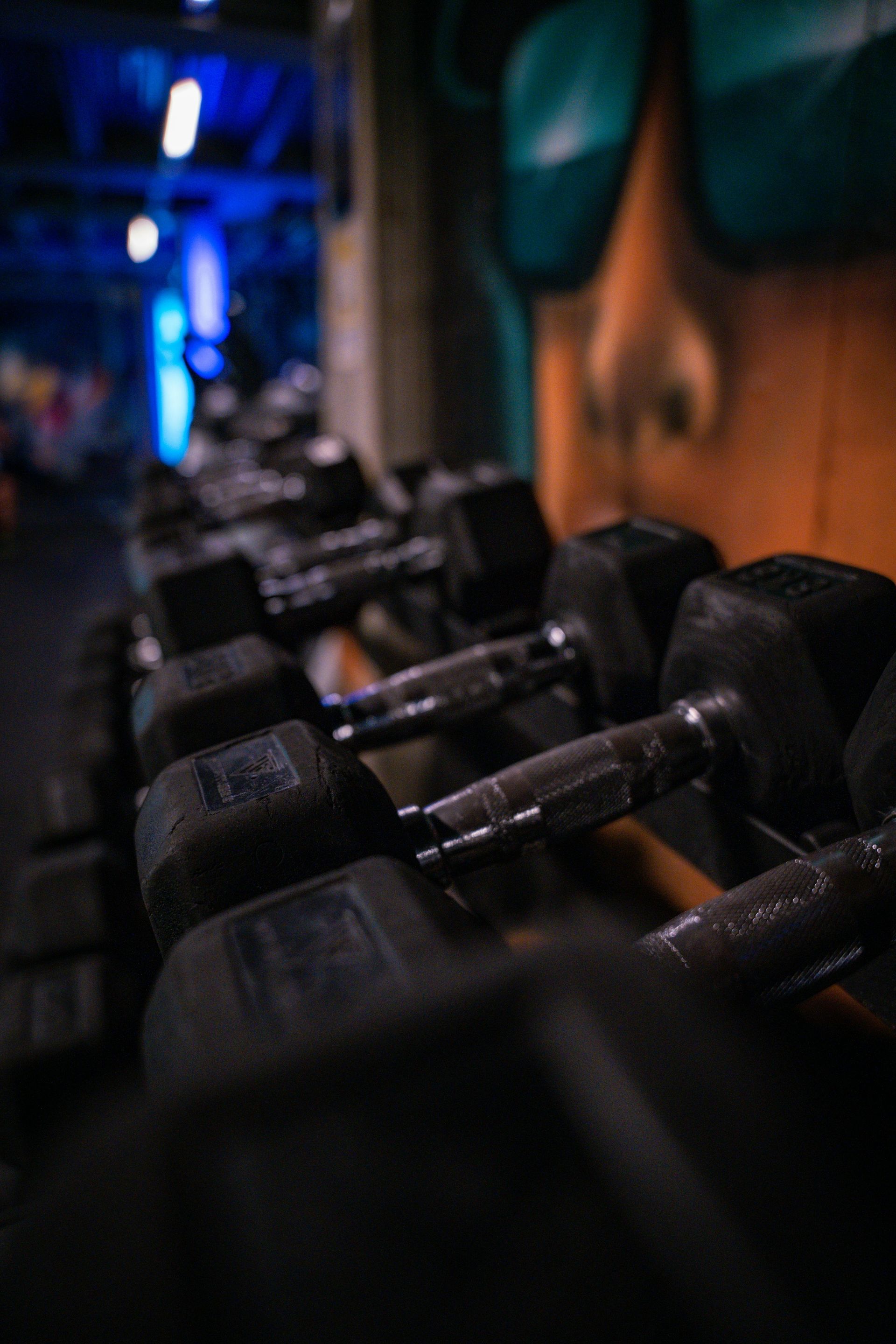 Interieur van een sportschool met fitnessapparaten, zwarte muren en neonverlichting.