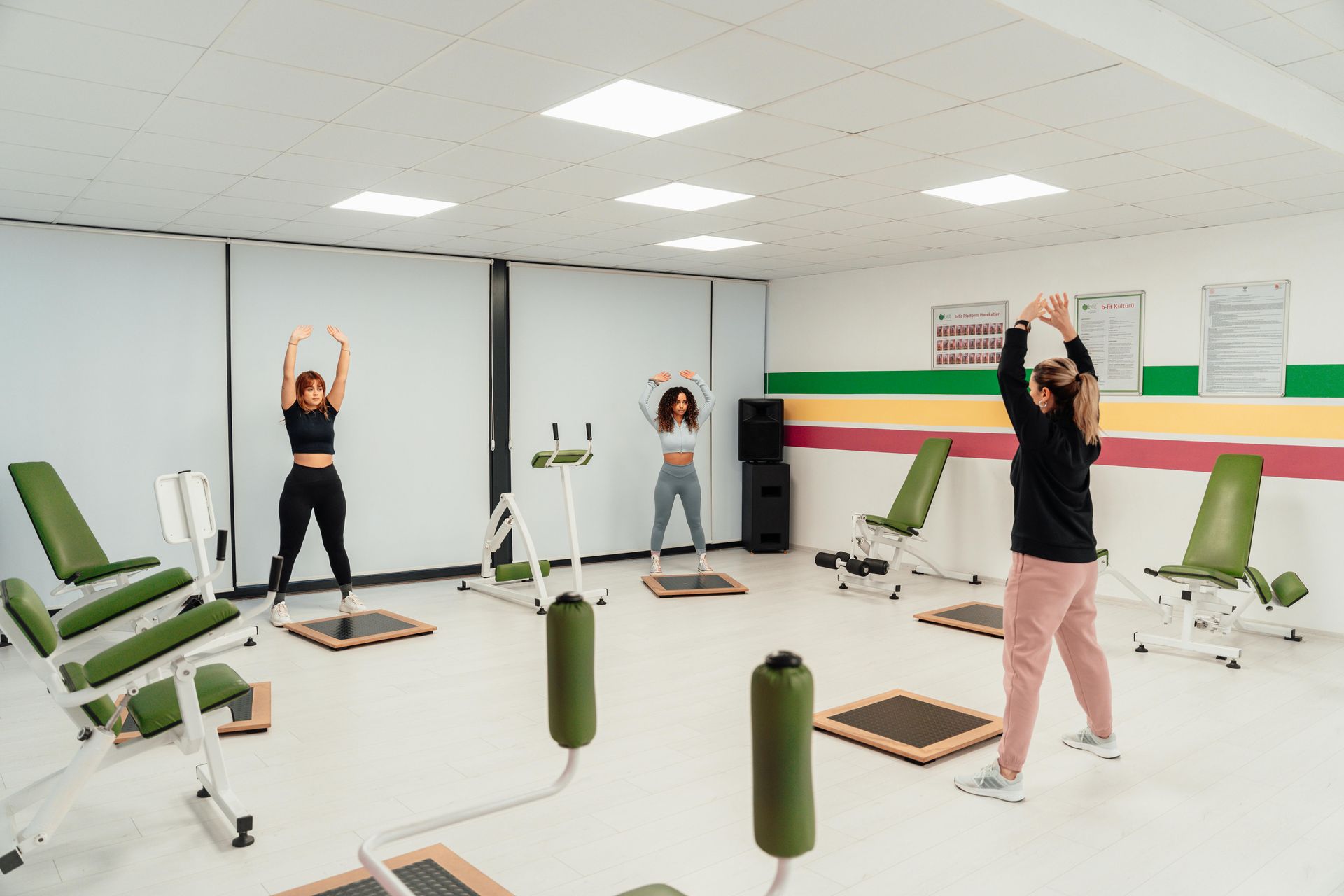 Vrouw die halter squats doet in een sportschool, gekleed in een felgroen shirt en een zwarte legging.