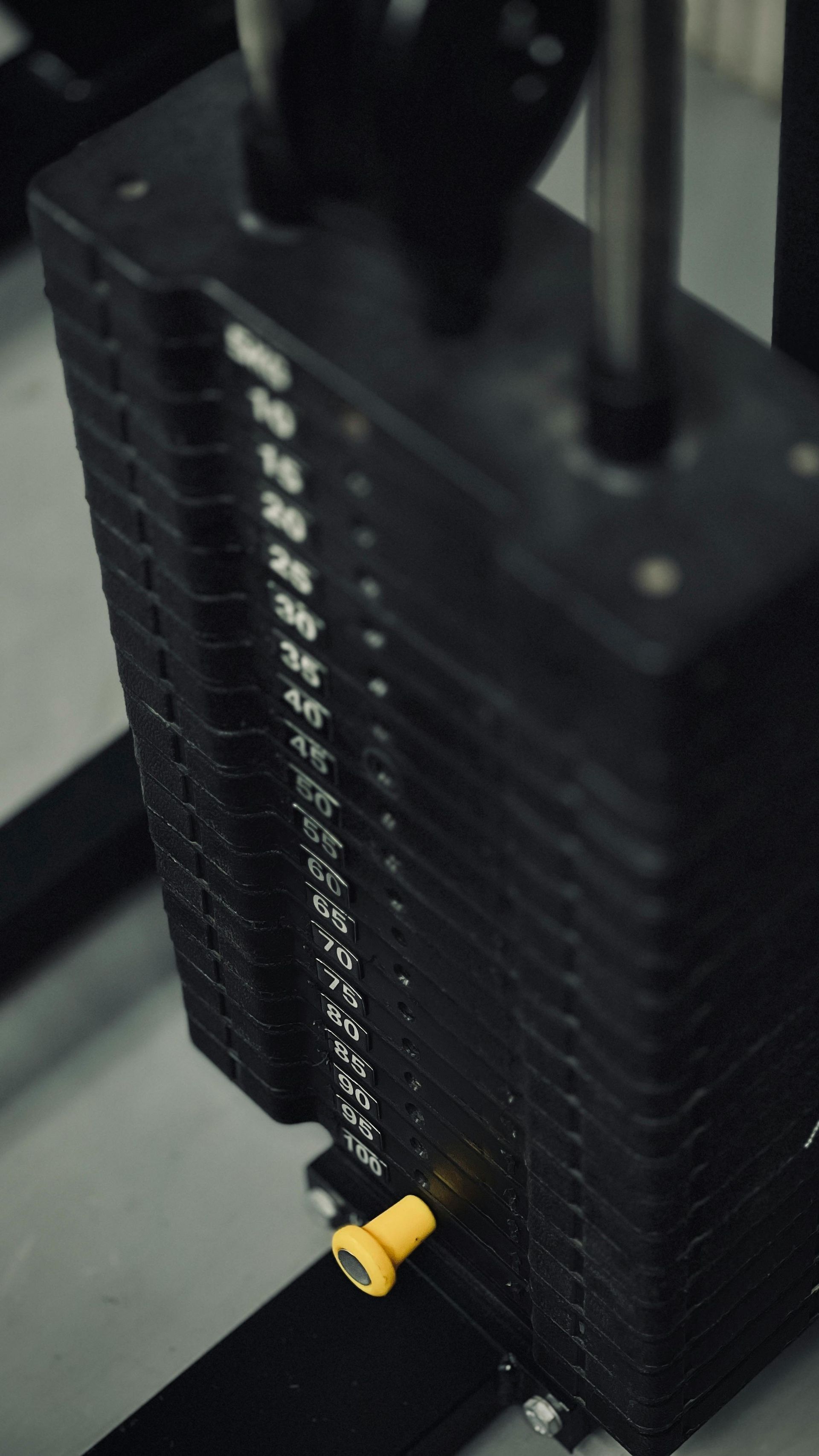 Vrouw gebruikt een fitnessapparaat onder begeleiding van een trainer in een sportschool, met zwarte en oranje accenten.