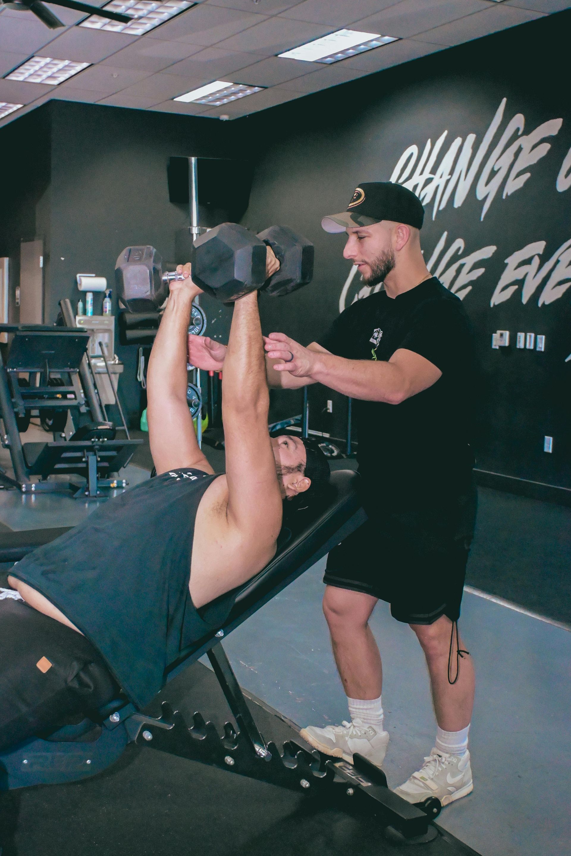 Vrouw doet een squat met een halter, onder begeleiding van een trainer in een sportschool.