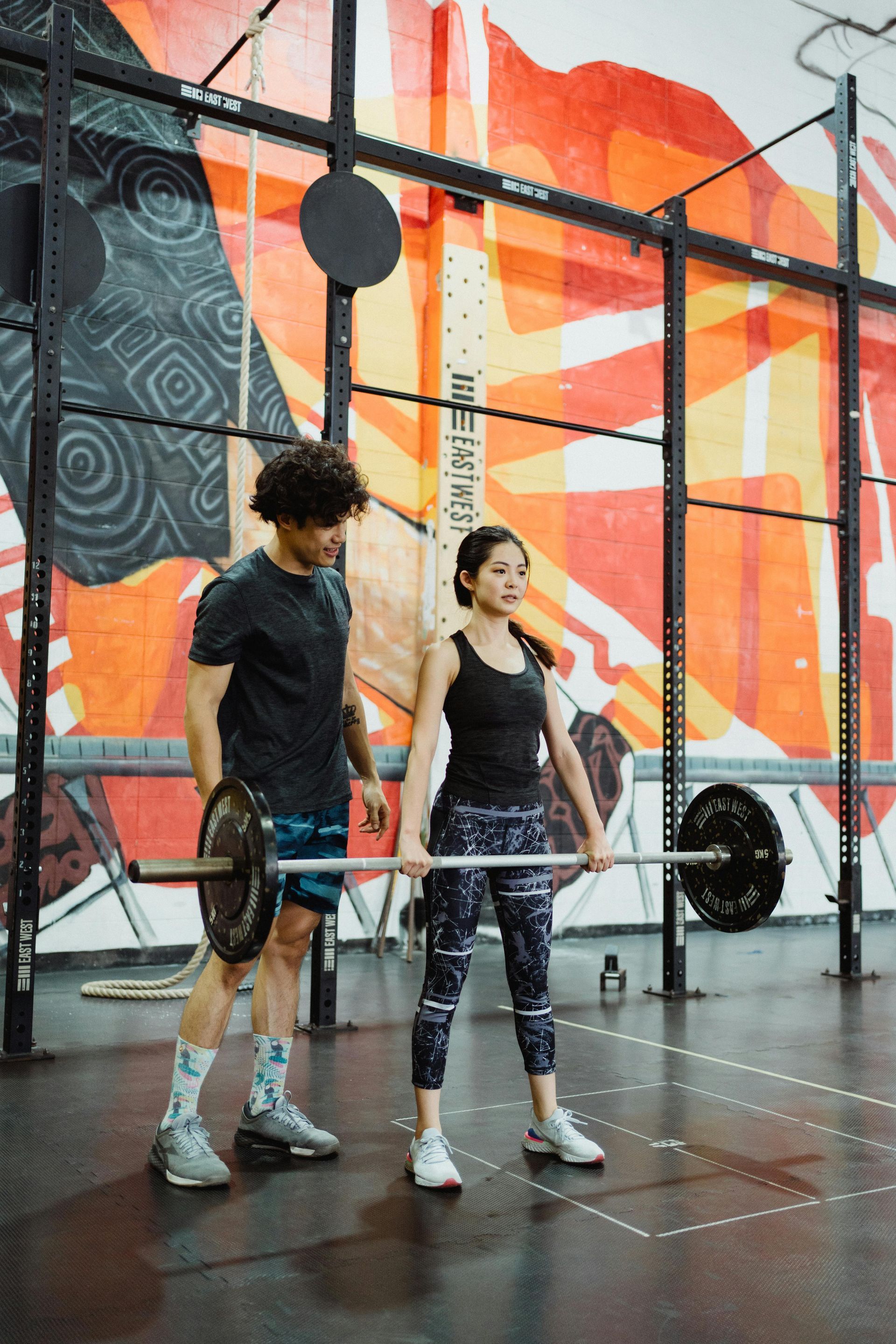 Vrouw doet een squat met een halter, onder begeleiding van een trainer in een sportschool. 
