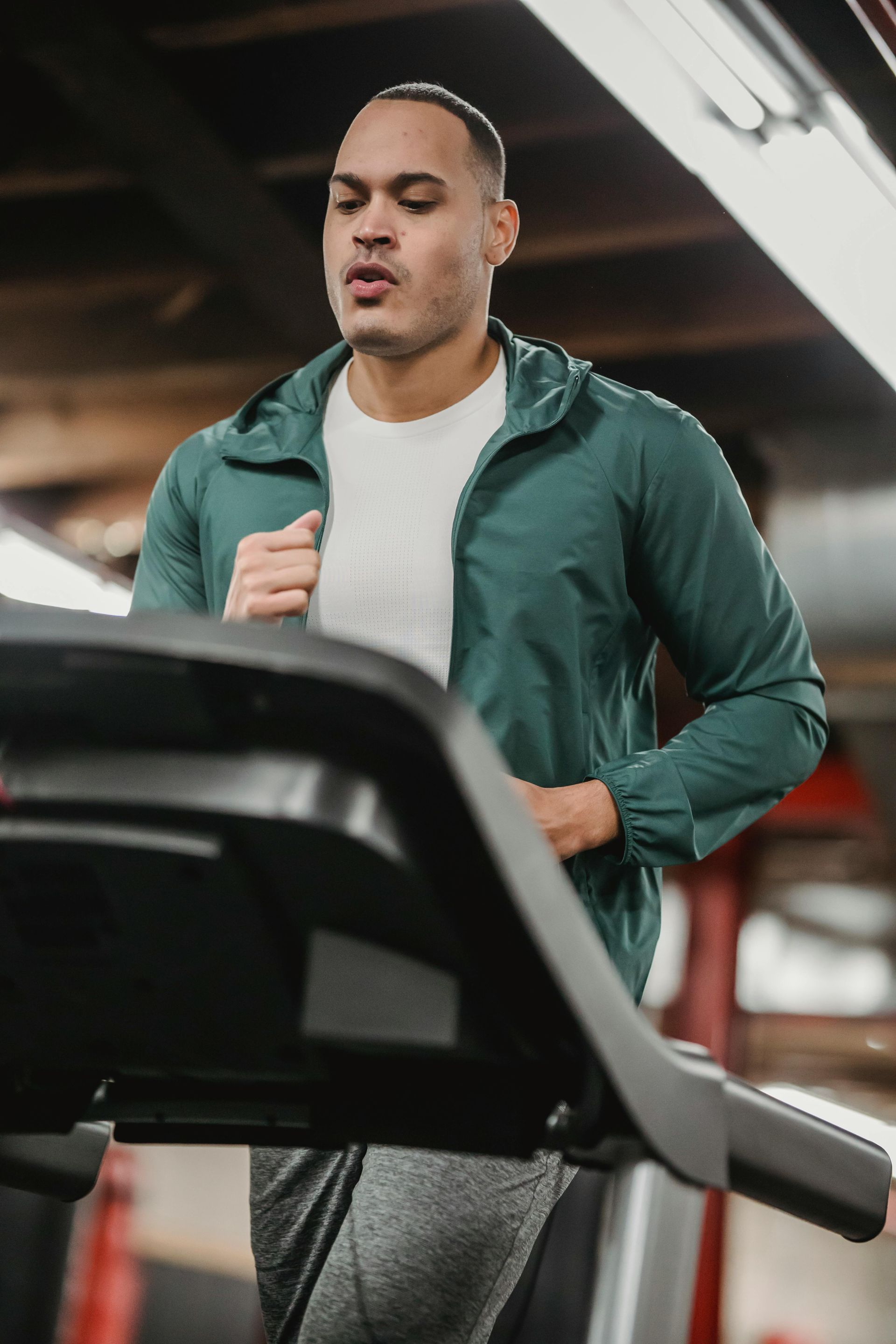 Vrouw op een fitnessapparaat, lachend naar een man die haar lijkt te helpen. Donkere ruimte, oranje accentverlichting.