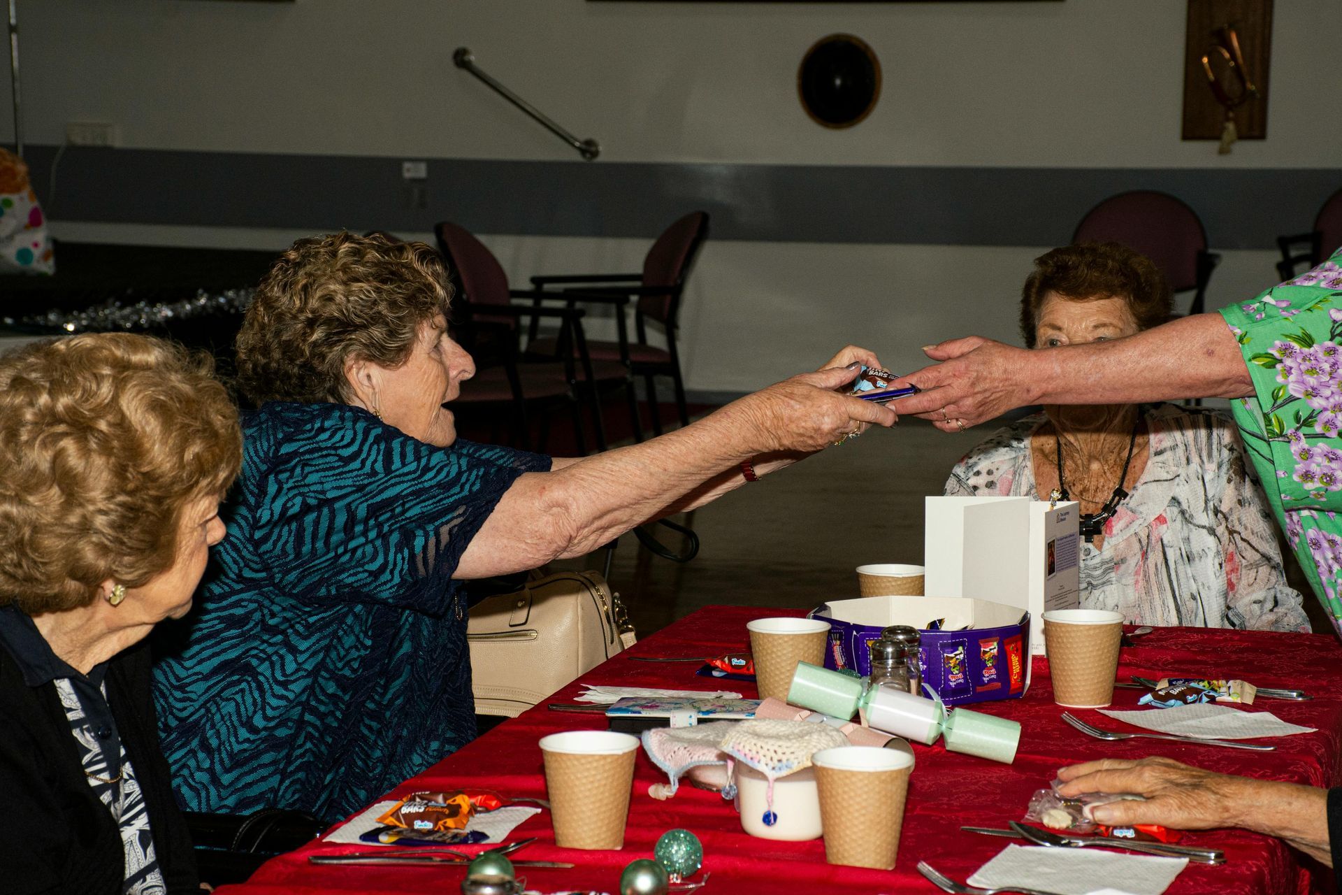 Two people reaching across a table to exchange items at a decorated indoor gathering