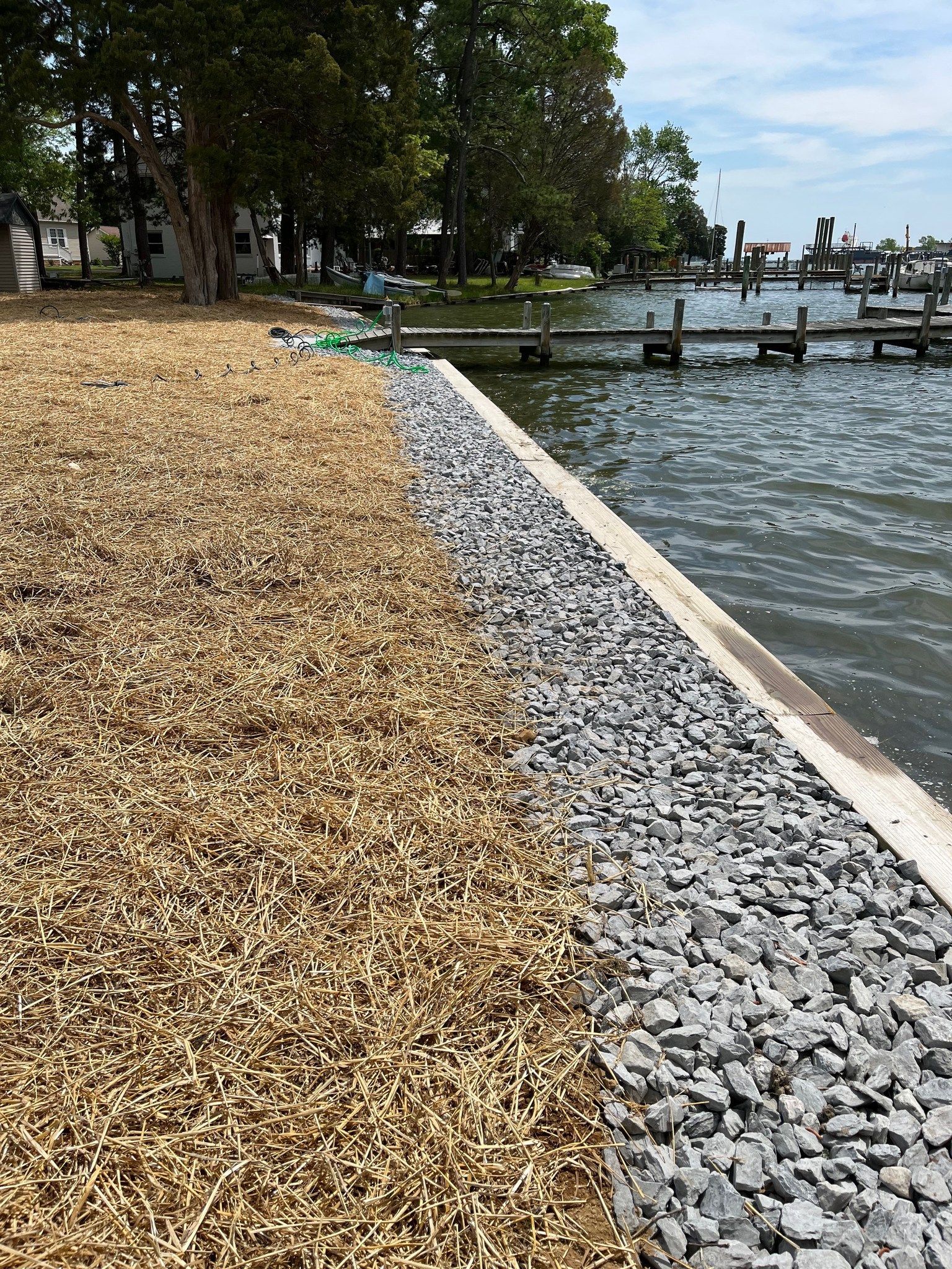 A shoreline with a gravel border separating a woodchip-covered area from the water and a wooden dock.