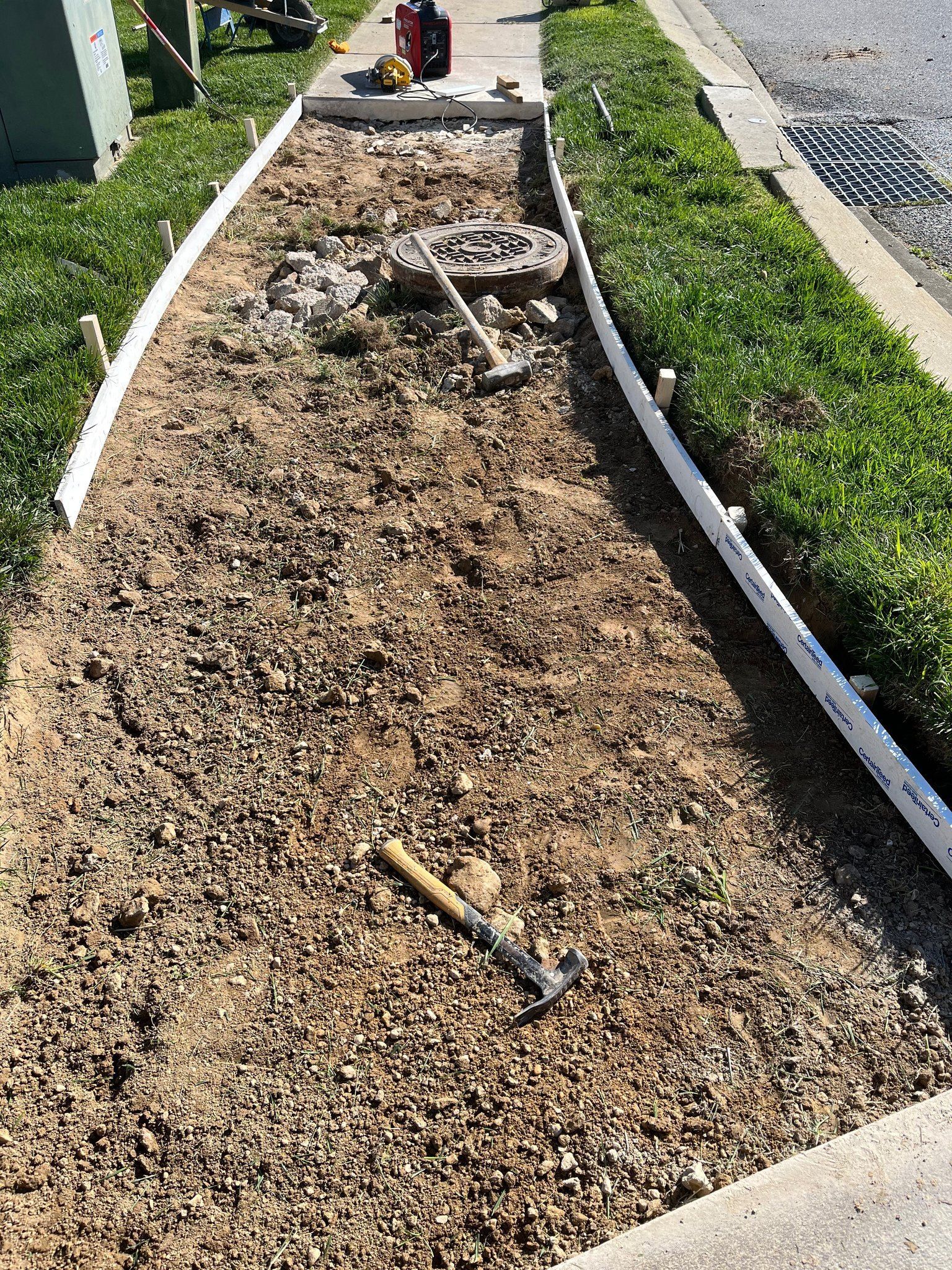 Concrete Contractor: A rectangular dirt pathway under construction, bordered by white wooden forms with tools .