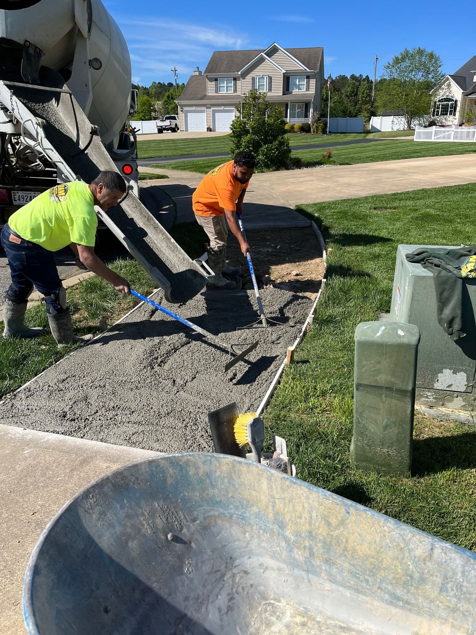 Pouring Concrete: Two construction workers pour and spread wet concrete from a truck into a sidewalk form.