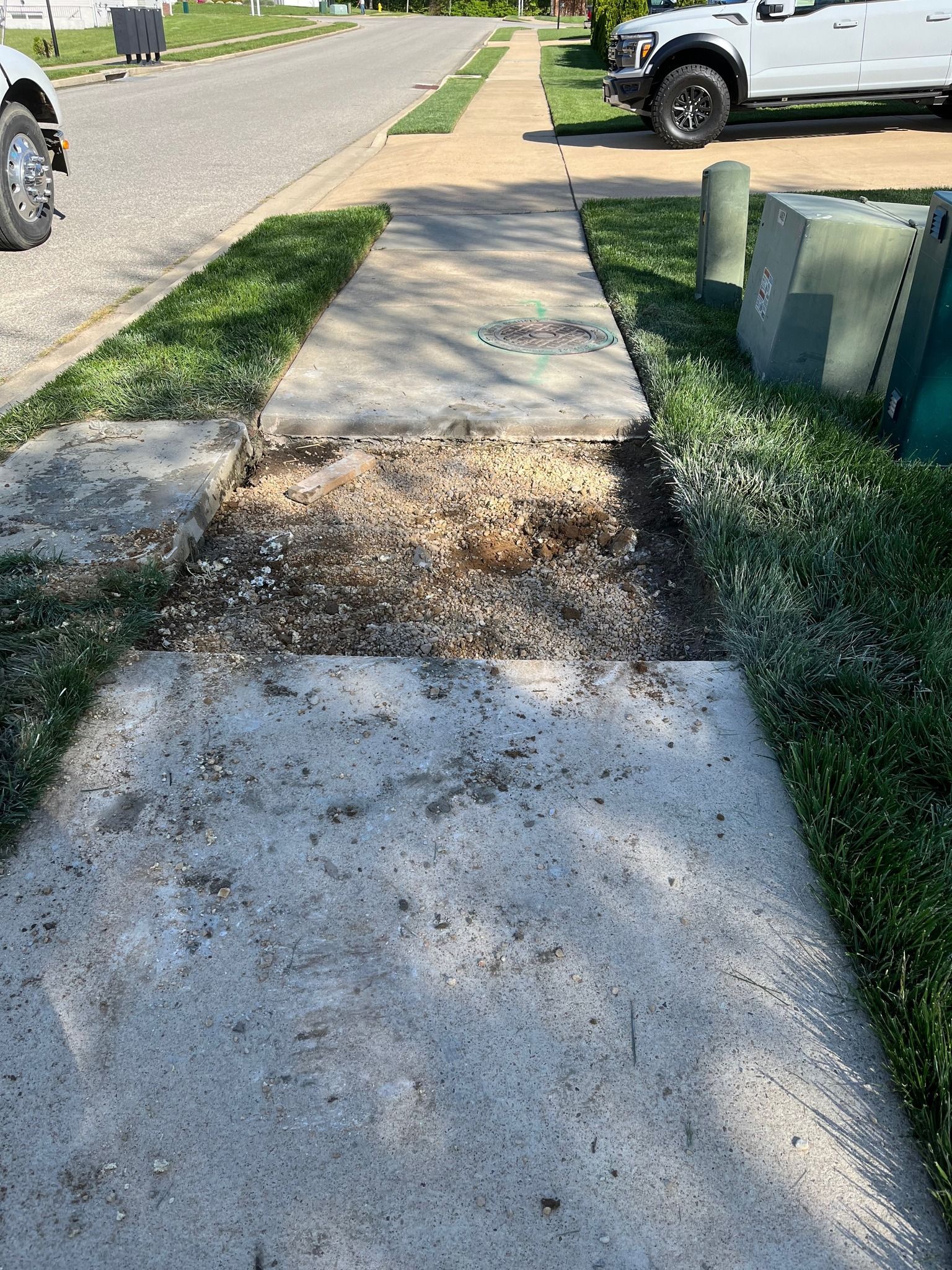 A section of concrete sidewalk is missing, leaving a patch of dirt and debris, creating a tripping hazard.