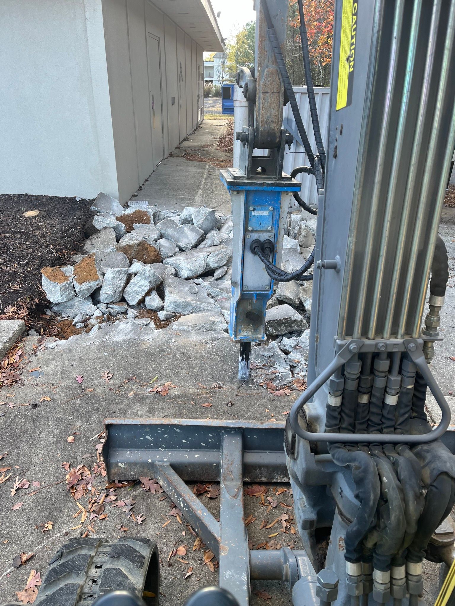 Demolition Southern MD: An excavator with a hydraulic breaker attachment sits on pavement near a pile of concrete rubble.