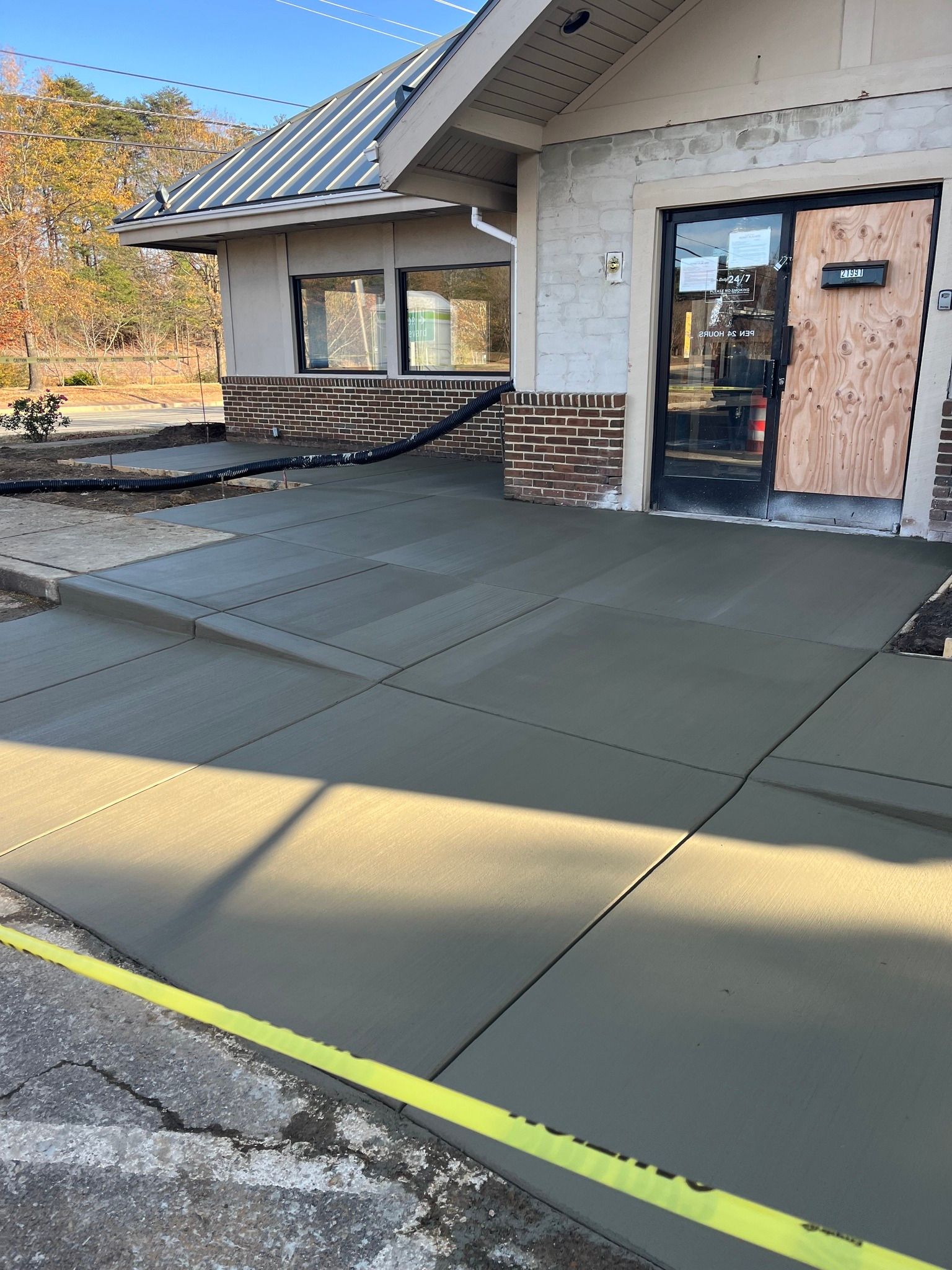 A newly poured concrete entryway ramp leading to a building entrance with a boarded-up door.