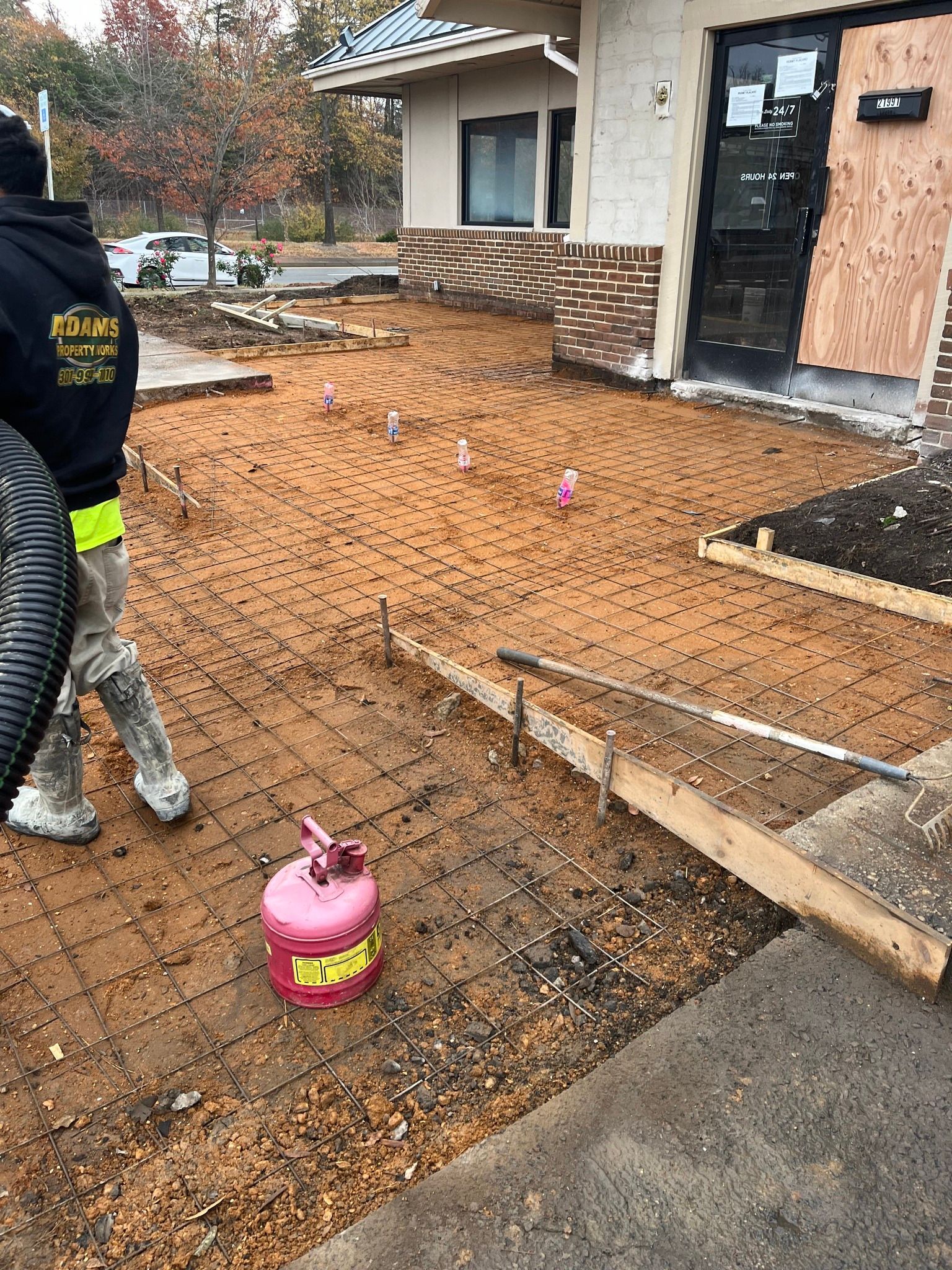 A construction worker stands on a dirt site with wire mesh laid out for a new concrete foundation in front of a building.