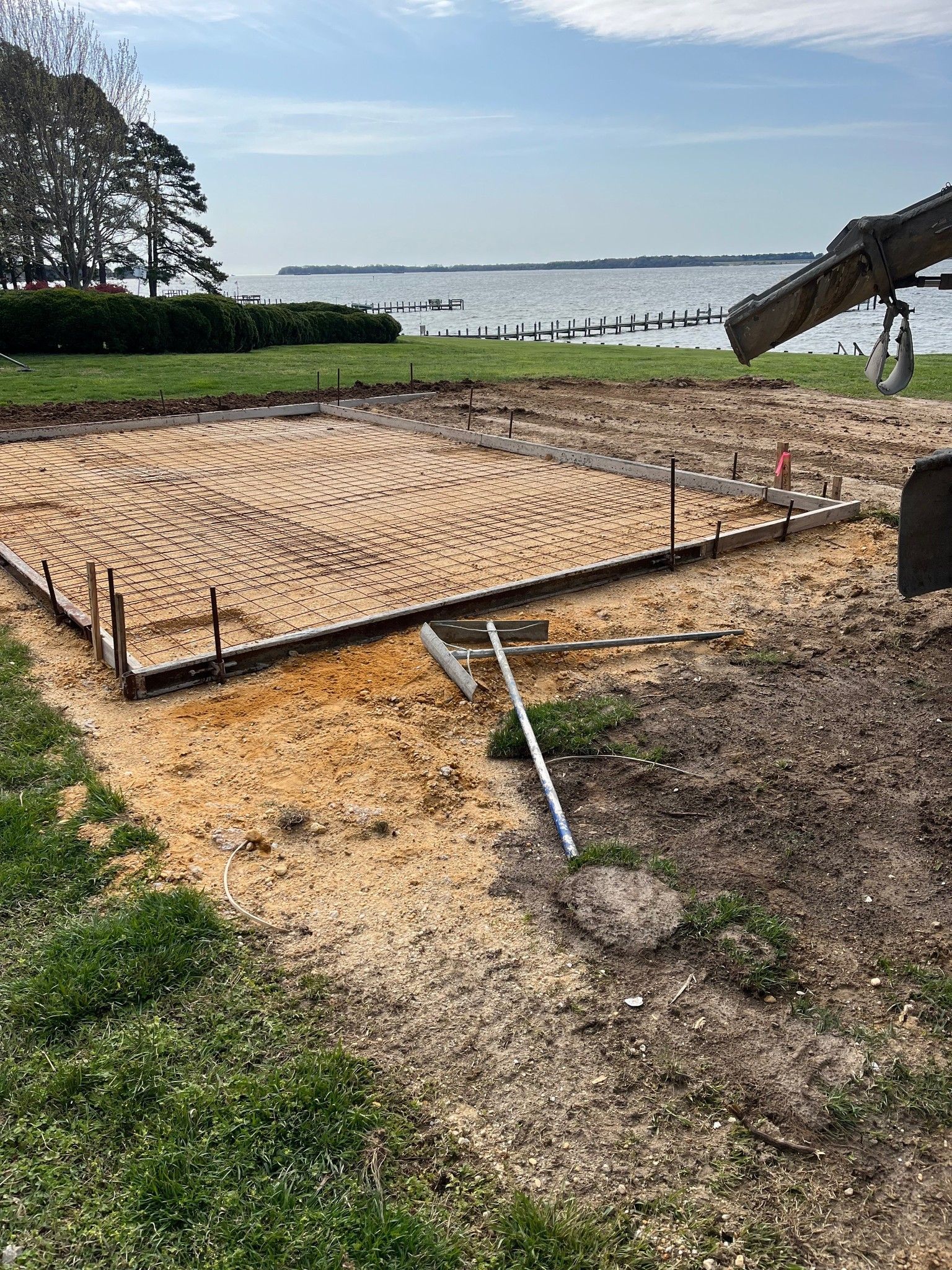 A rectangular foundation site with coiled radiant heating tubing, set on a grassy bank overlooking a large body of water.