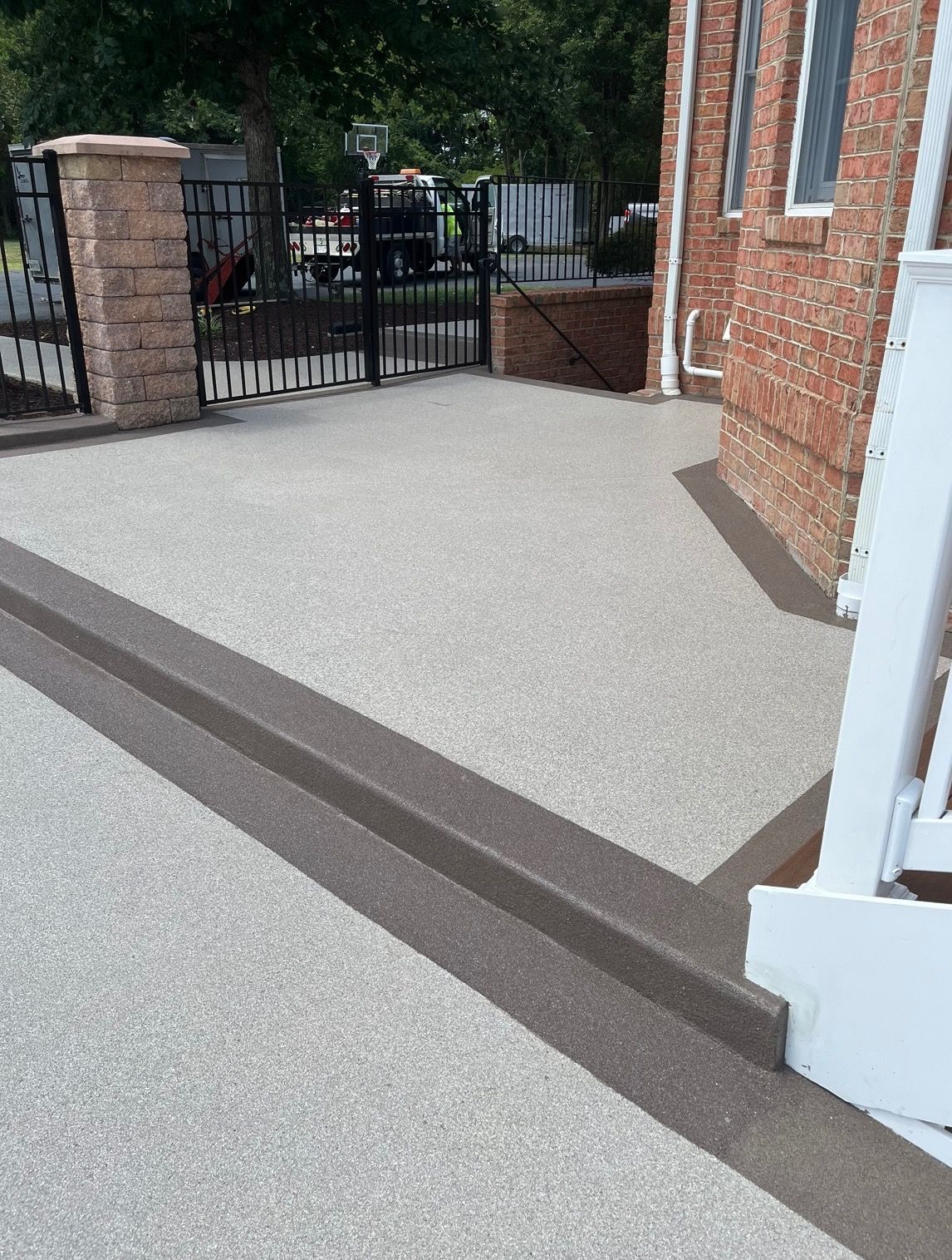 A light-colored textured patio surface featuring a darker brown border and a step leading up to a brick building.