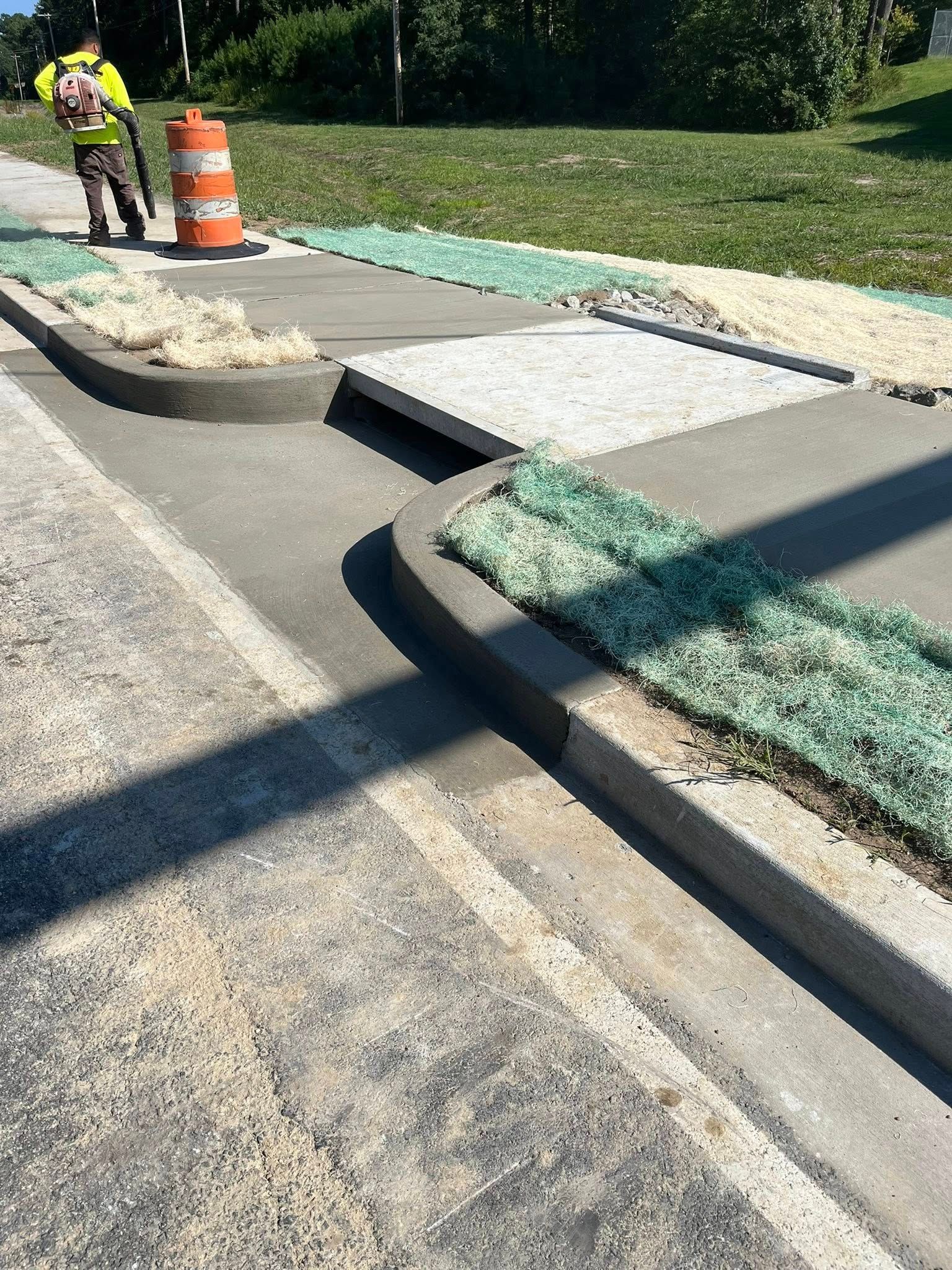 A worker in a yellow vest uses a blower near a concrete curb transition that creates a significant, uneven gap.