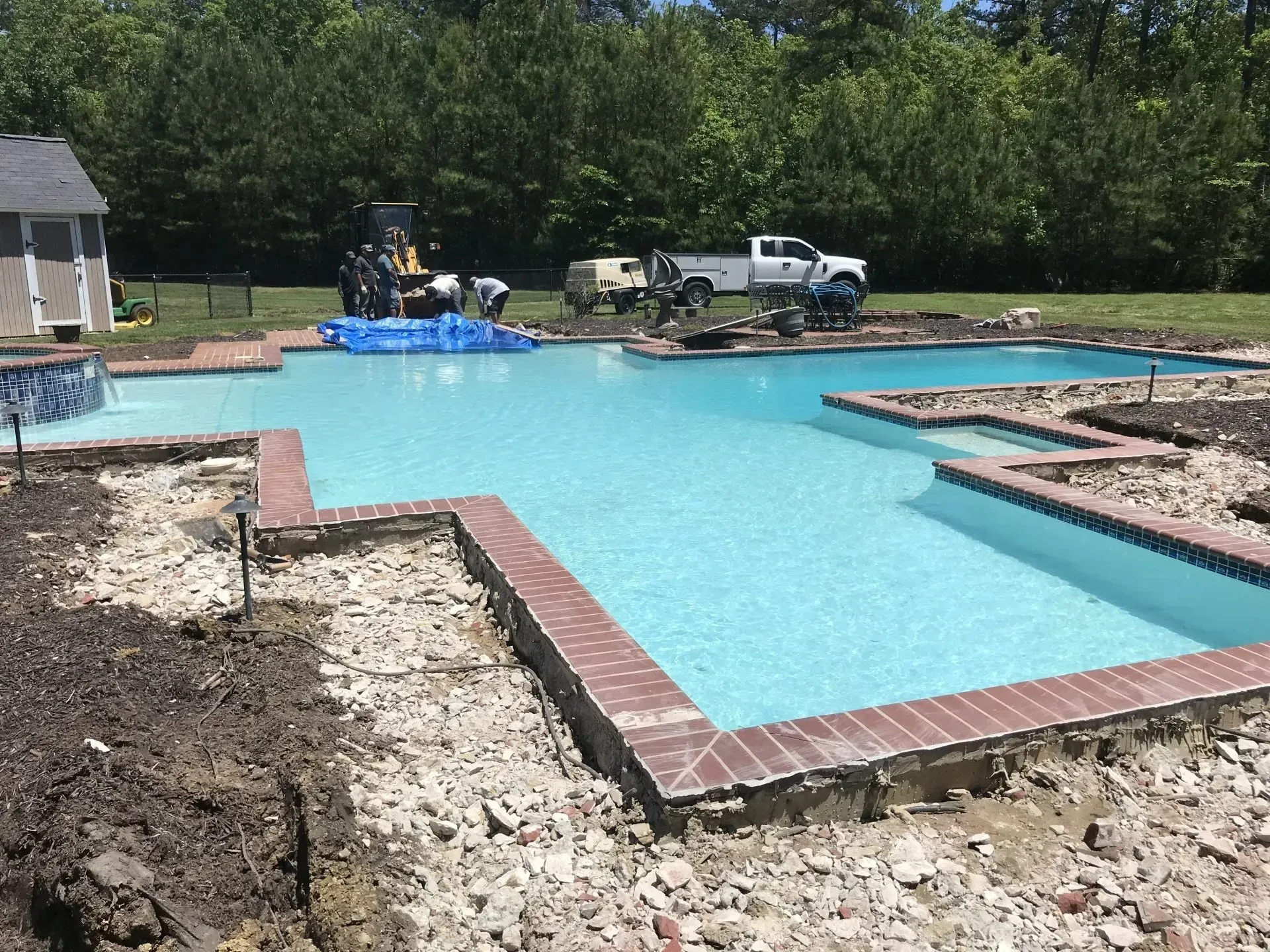 Concrete Patio Construction workers building a brick-trimmed swimming pool in a backyard on a sunny day.
