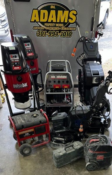 Collection of industrial concrete grinding equipment & tools arranged in front of a trailer branded DL Adams Property Works.