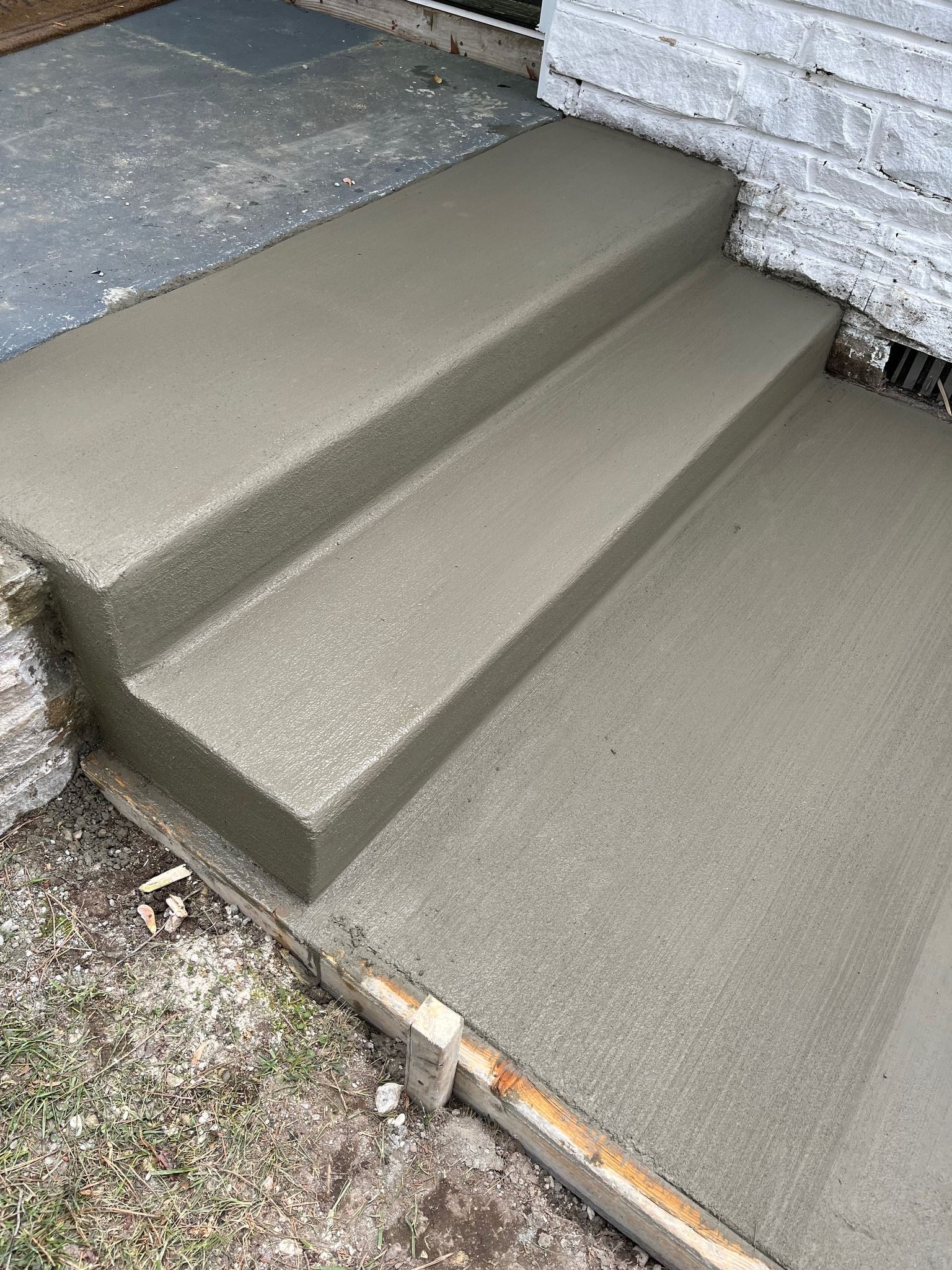 Newly poured gray concrete steps and a landing leading up to a white brick building, with wooden form boards still visible.