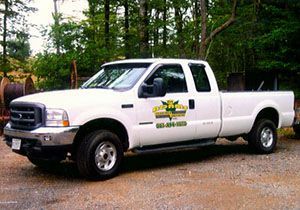 A white Ford Super Duty pickup truck parked on a gravel lot in front of a line of trees.