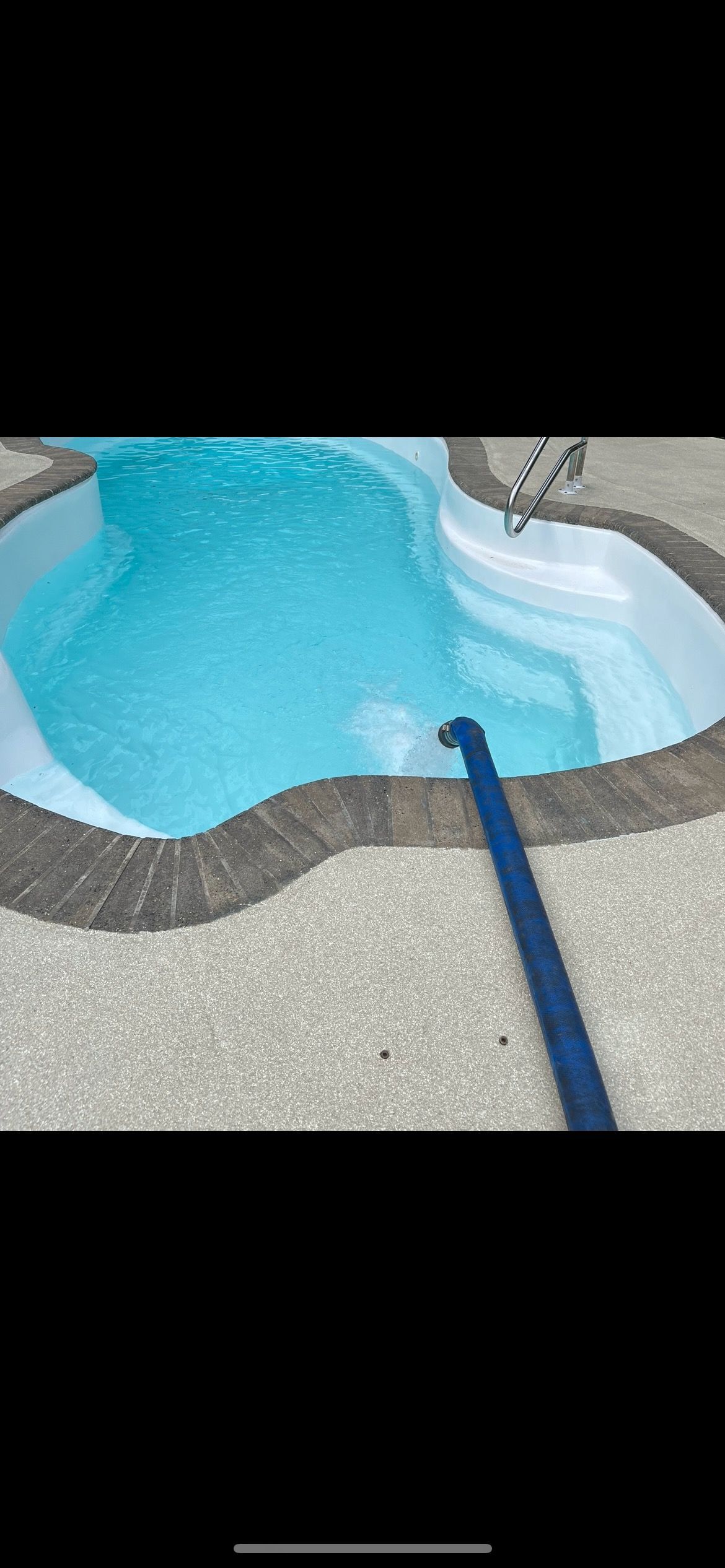 A turquoise swimming pool with a stone border and a blue hose submerged in the water.