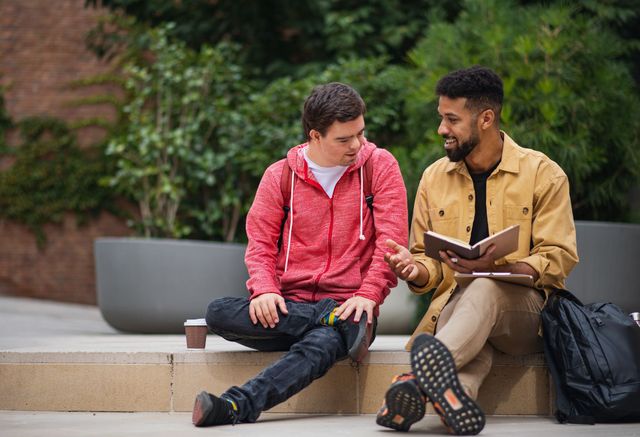 Two men are sitting on a bench reading a book.